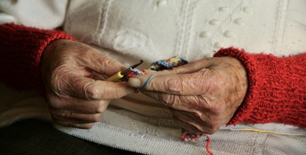 Eine alte Frau strickt. Zu sehen sind ihre Hände.